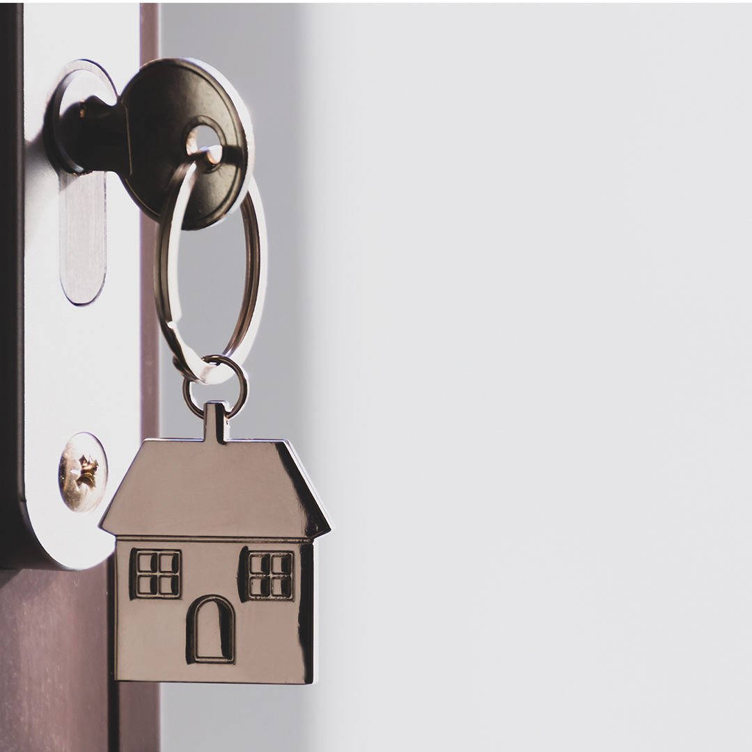 1080x1080Social-3 A close up shot of a key in a door with a silver house shaped keychain hanging from it