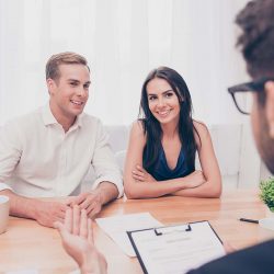 A young couple sits across a desk from a realtor who is helping them sell their home.