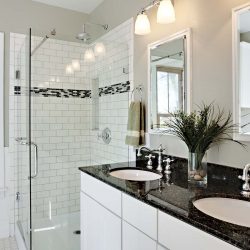 A nicely renovated, bright white remodeled bathroom with a glass shower and granite countertops.